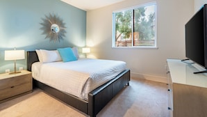 A bedroom with a bed, bedside tables, a TV, and a window with a view of trees.