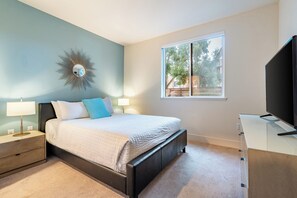 A bedroom with a bed, bedside tables, a TV, and a window with a view of trees.