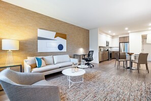 A modern living room with a sofa, coffee table, and chairs, a dining area with a table and chairs, and a kitchen with appliances and cabinets.
