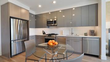 A modern kitchen with stainless steel appliances, a glass dining table, and grey cabinetry.