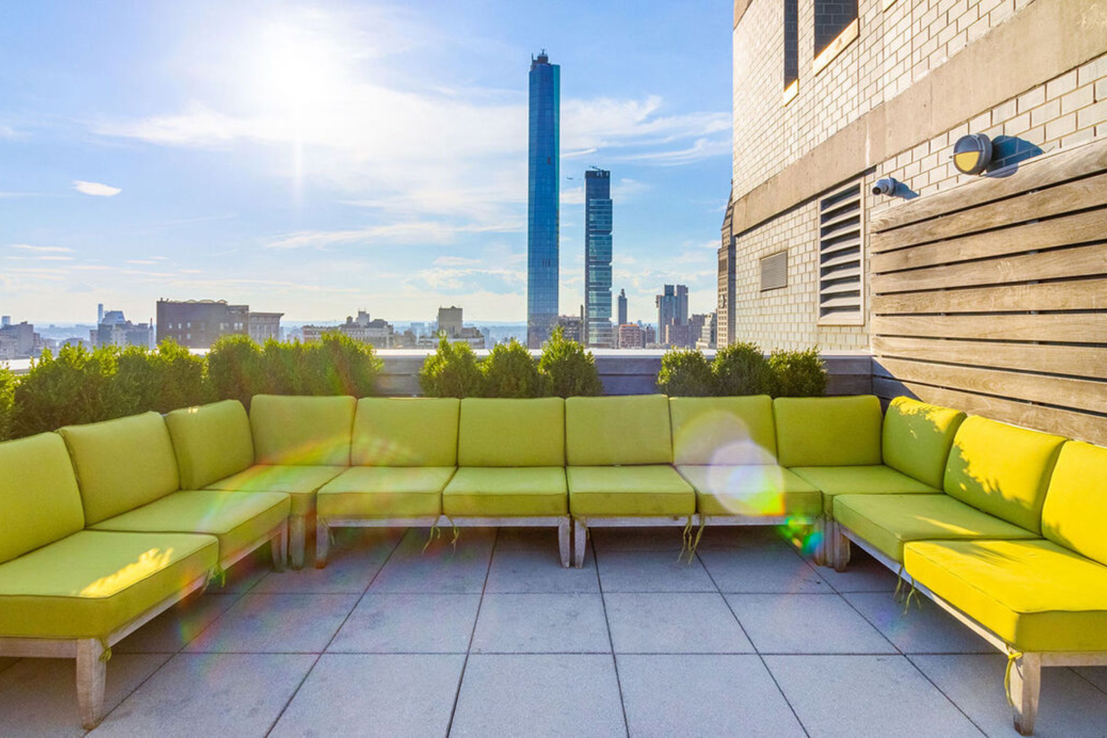 A rooftop terrace with a green sofa set, a view of a city skyline, and a building with a brick facade.