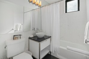 Un baño moderno con inodoro blanco, lavabo con encimera negra, espejo grande y cortina de ducha.
