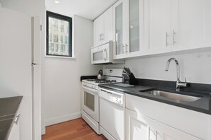 A modern kitchen with white cabinetry, a stainless steel sink, and a built-in microwave. - Chic Gramercy Retreat | W/D, Rooftop Deck (New York)