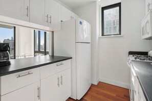 Una cocina moderna con armarios blancos, encimera negra, estufa de acero inoxidable y ventana con vista a la ciudad.