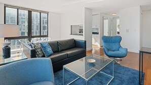 A modern living room with a glass coffee table, a black leather sofa, a blue armchair, and a glass dining table.