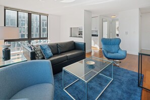 A modern living room with a glass coffee table, a black leather sofa, a blue armchair, and a glass dining table. - Chic Gramercy Retreat | W/D, Rooftop Deck (New York)