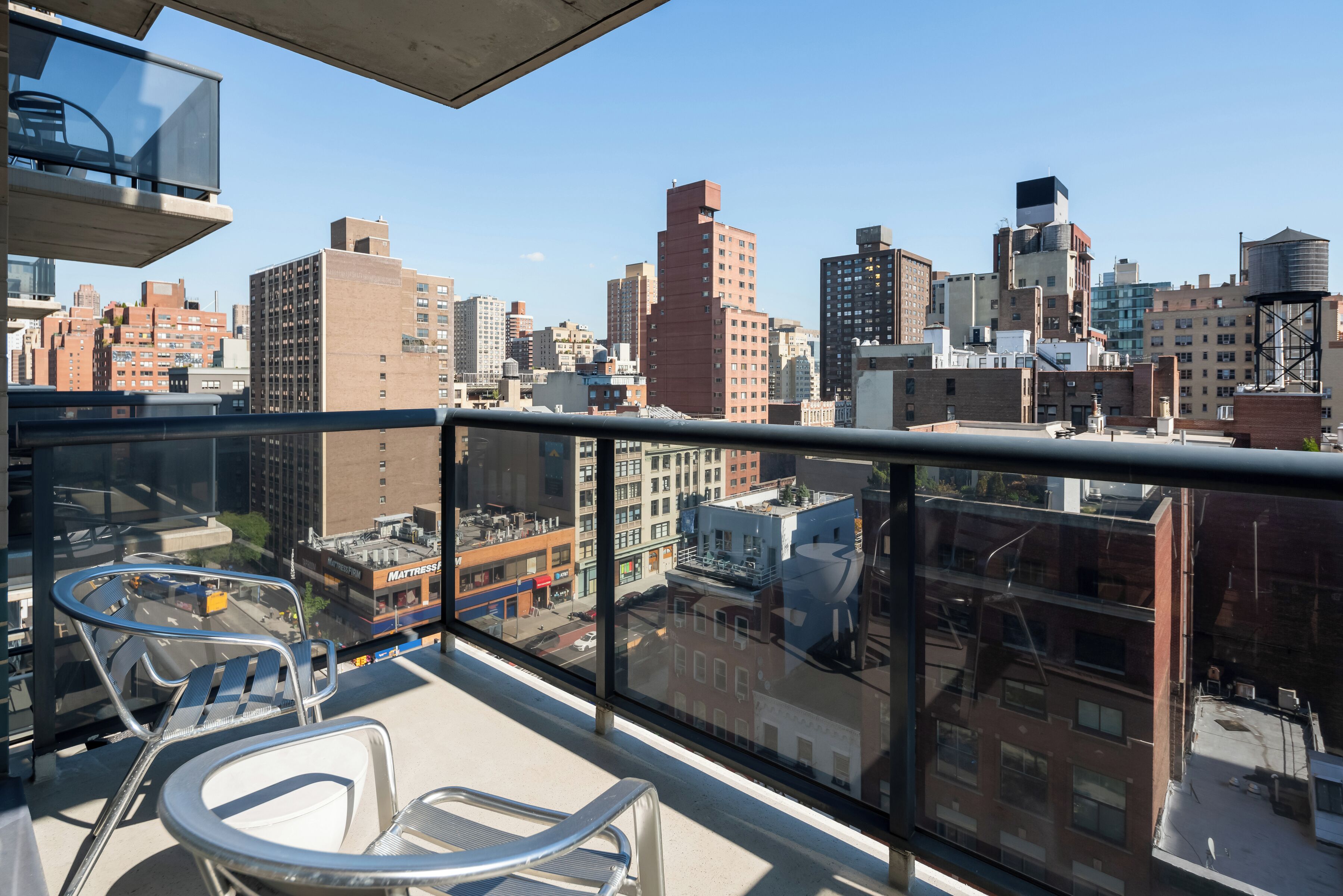 A balcony with a city view, metal chairs, and a glass railing.