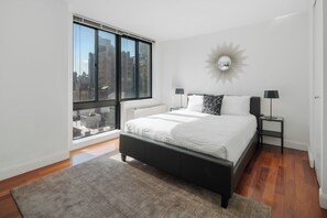 Un dormitorio moderno con un ventanal grande, una cama, una mesita de noche y un espejo montado en la pared.
