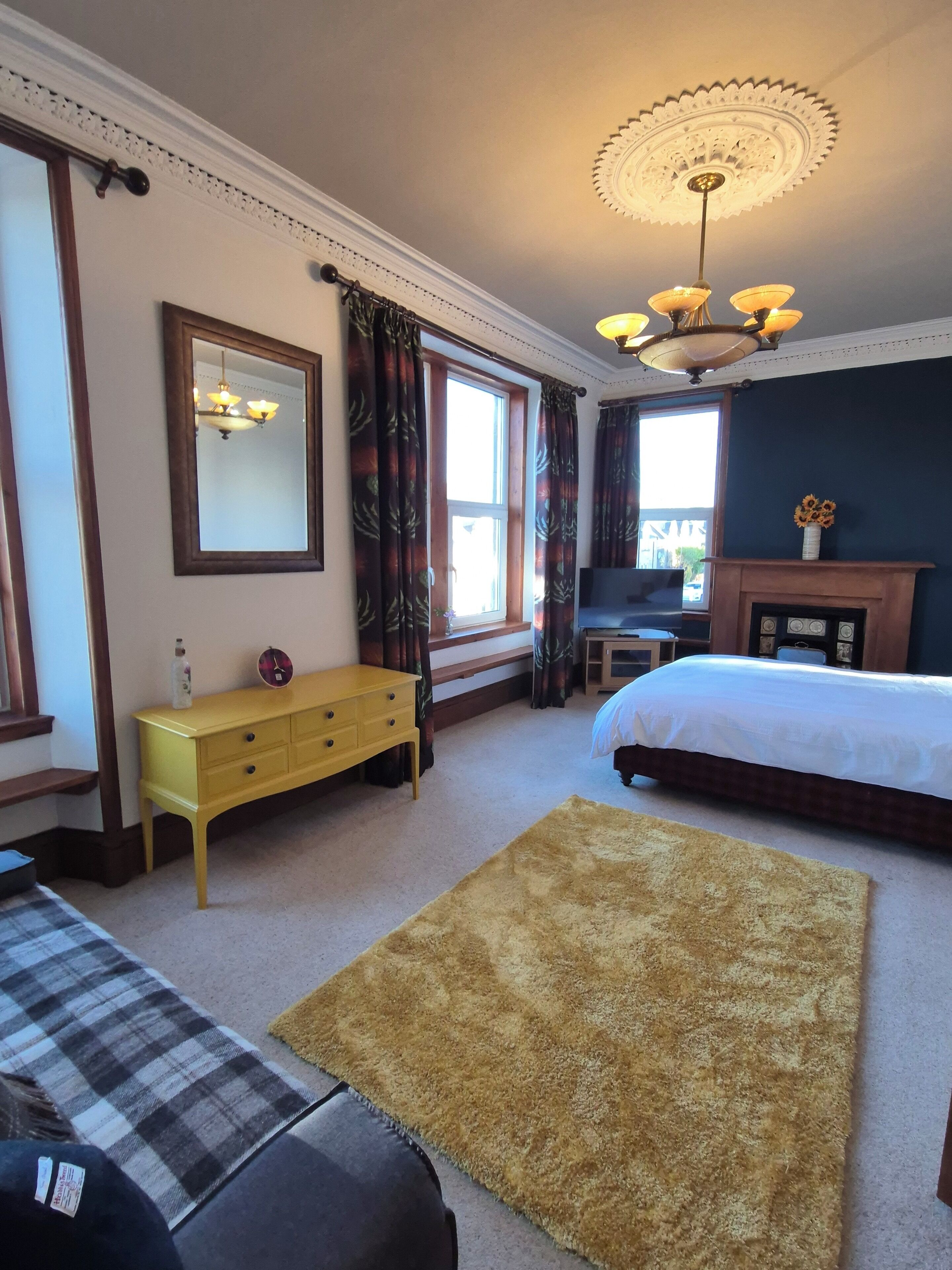A bedroom with a bed, a dresser, a mirror, a fireplace, and a window with curtains.