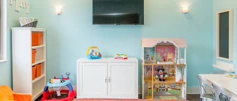 A children's playroom with a television mounted on the wall, a playpen, a dollhouse, and a colorful rug.