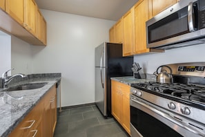 A kitchen with wooden cabinets, a stainless steel refrigerator, a microwave, a gas stove, and a granite countertop.