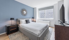 A modern bedroom with a bed, bedside tables, a mirror, and a window with a view of buildings. - Bright Midtown West Living | W/D, Fitness Center (New York)