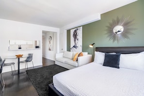 A modern hotel room with a large bed, a white sofa, a dining table with chairs, and a kitchen area. - Stay in the UES | Pet-Friendly, On-Site Laundry (New York)