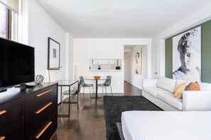 A modern hotel room with a large bed, a TV, a desk with chairs, and a dining area. - Stay in the UES | Pet-Friendly, On-Site Laundry (New York)