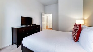Un dormitorio con una cama, un televisor sobre un aparador, una lámpara y una puerta que da a otra habitación.
