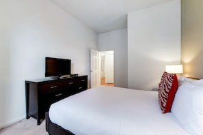 Una camera da letto con un letto, una TV sopra un comò, una lampada e una porta che dà su un'altra stanza.