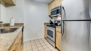 Una cocina compacta con refrigerador de acero inoxidable, microondas, estufa y encimera de granito.