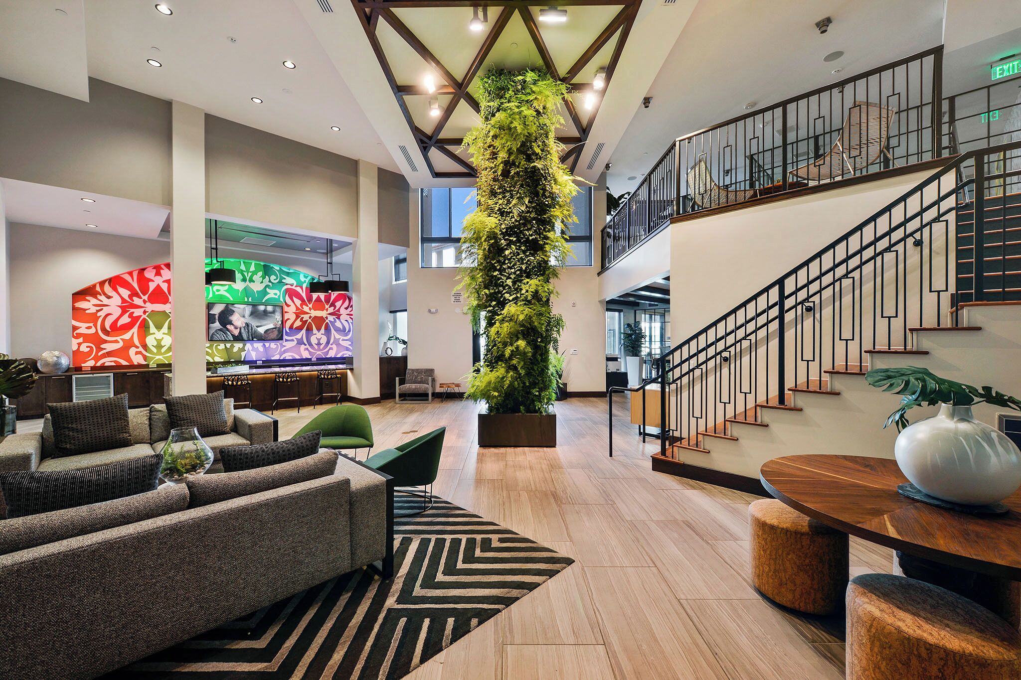 A spacious lobby with a high ceiling, a large vertical garden, a staircase, and a seating area with sofas and a coffee table.