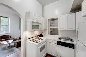 A modern kitchen with white cabinets, a gas stove, a microwave, a dishwasher, and a sink. - Central Park Living | UWS | On-Site Laundry (New York)
