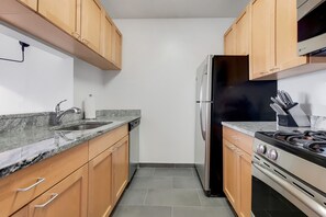 Una cocina con gabinetes de madera, un refrigerador de acero inoxidable, una estufa a gas y una encimera de granito.