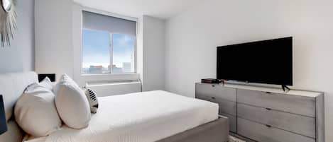 A modern bedroom with a large bed, a TV, and a city view.