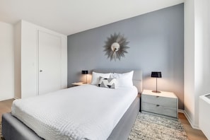 A bedroom with a bed, nightstands, a wall-mounted mirror, and a door.