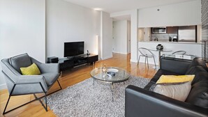 Uma sala de estar moderna com televisão de tela plana, uma poltrona cinza, um sofá de couro preto e uma mesa de centro de vidro.