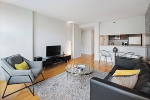Ein modernes Wohnzimmer mit einem Flachbildfernseher, einem grauen Sessel, einem schwarzen Ledersofa und einem Glastisch.