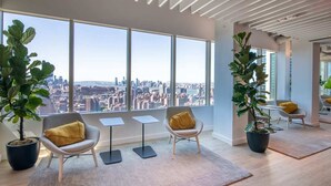 Um interior moderno com grandes janelas, duas plantas em vasos e vista para a cidade.
