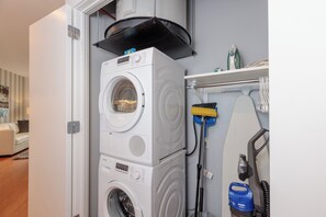 A compact laundry area with stacked washing machines, a vacuum cleaner, and ironing equipment.