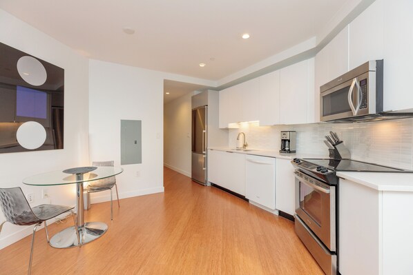 A modern kitchen with white cabinets, stainless steel appliances, and a glass dining table.