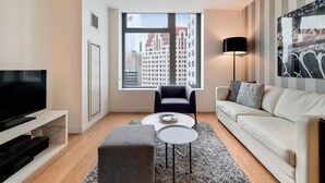A modern living room with a large window, a flat-screen TV, a sofa, a coffee table, and a lamp. - Modern 1 Bedroom in Downtown Boston (Boston)