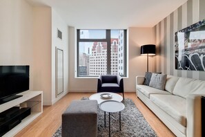 A modern living room with a large window, a flat-screen TV, a sofa, a coffee table, and a lamp. - Modern 1 Bedroom in Downtown Boston (Boston)