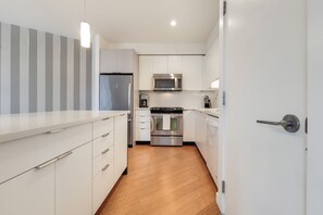 A modern kitchen with white cabinetry, stainless steel appliances, and a wooden floor. - Modern 1 Bedroom in Downtown Boston (Boston)