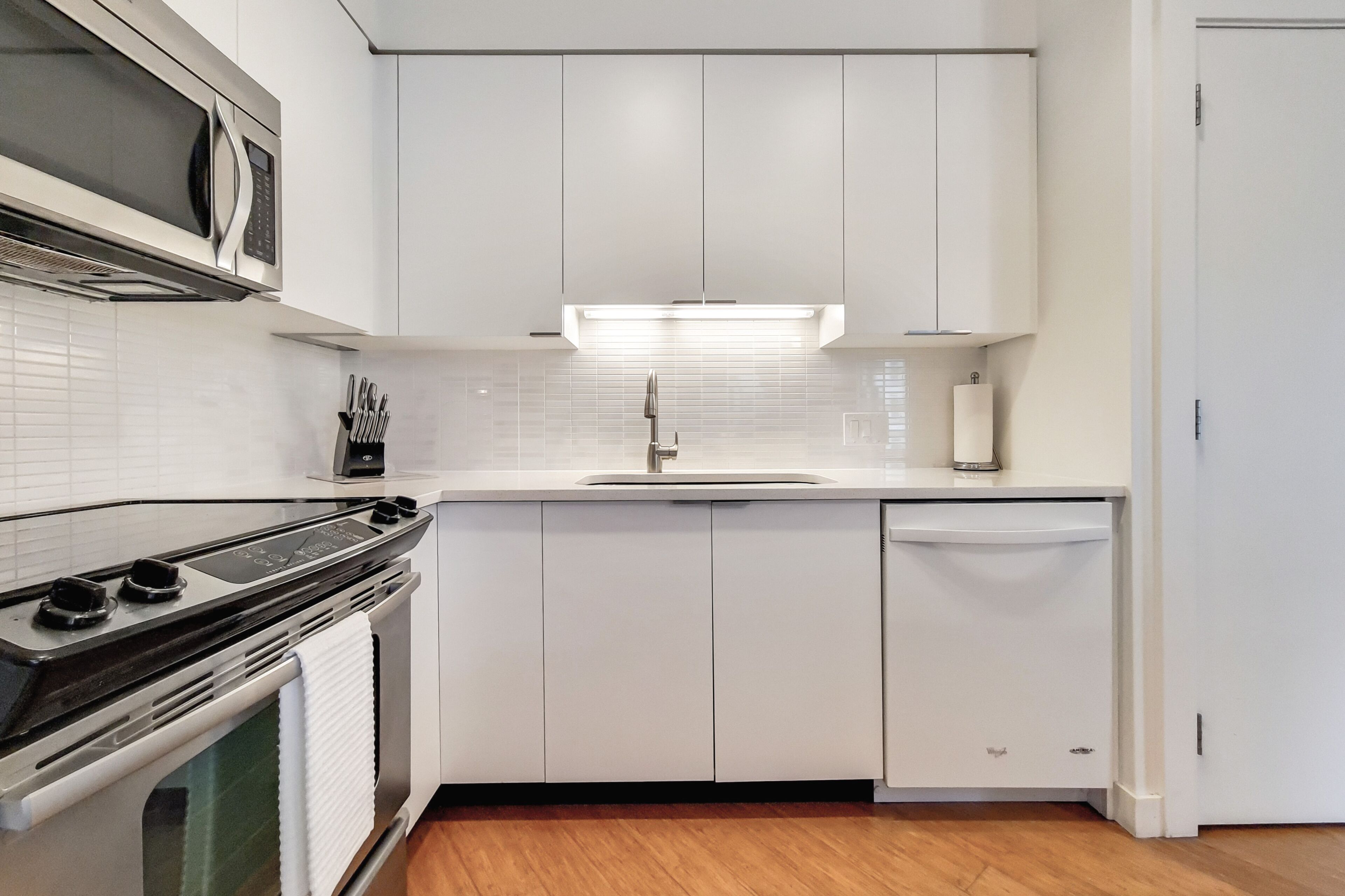 A modern kitchen with white cabinets, a stainless steel stove, a microwave, and a dishwasher.