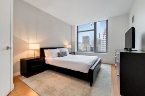 A modern bedroom with a large bed, bedside lamps, a dresser, and a TV.
