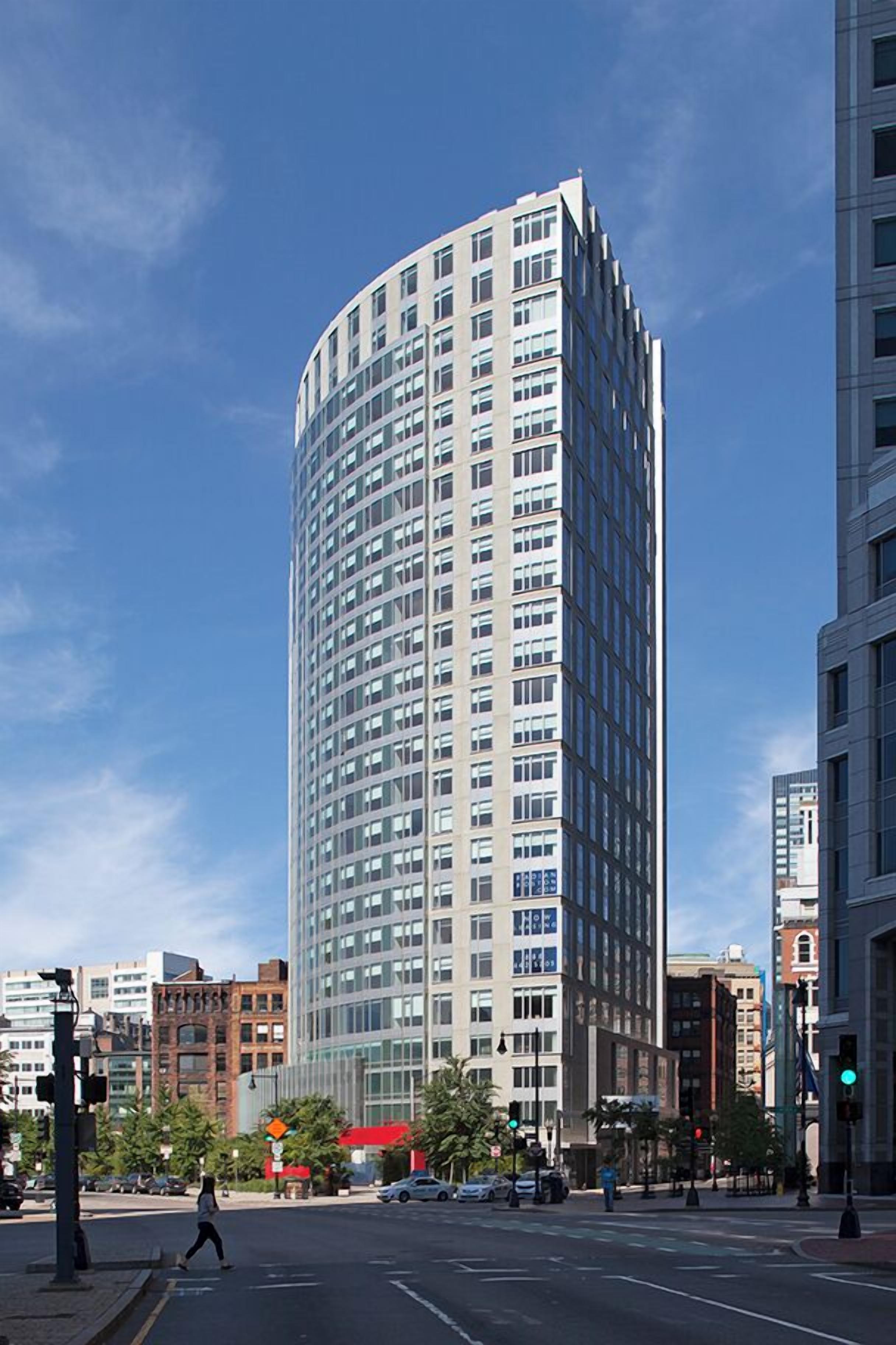 A tall, modern building with a curved facade, surrounded by other urban structures.