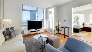 A modern living room with a flat-screen TV, white sofa, and a dining area with a small table and chairs.
