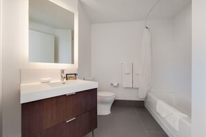 Um banheiro moderno com pia branca, toucador de madeira escura, vaso sanitário e banheira.