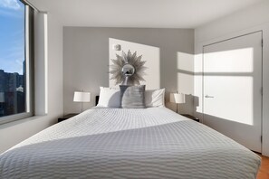 A modern hotel room with a large bed, a sunburst mirror above the headboard, and a city view through the window. - Chic 1 bed in Financial District (Boston)