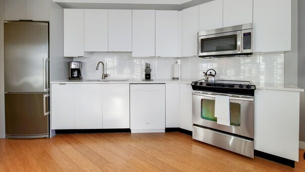 A modern kitchen with white cabinets, stainless steel appliances, and a wooden floor.