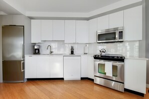 A modern kitchen with white cabinets, stainless steel appliances, and a wooden floor. - Chic 1 bed in Financial District (Boston)