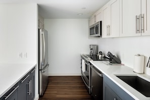 A modern kitchen with stainless steel appliances, white cabinetry, and a wooden floor. - Modern Two Bedroom with Views in Cambridge (Cambridge)