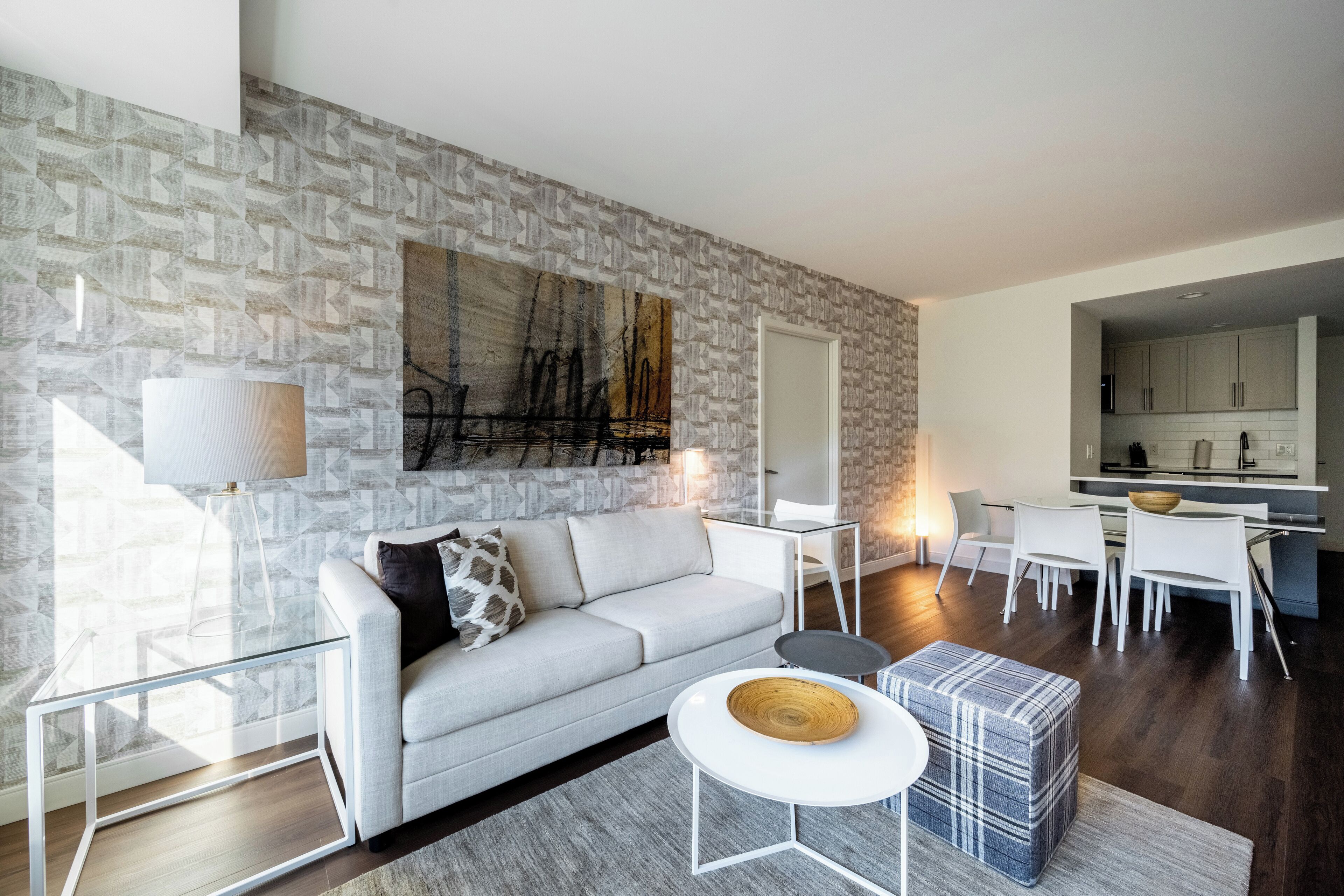 A modern living room with a grey sofa, a coffee table, and a dining area with white chairs and a kitchen in the background.