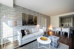 A modern living room with a grey sofa, a coffee table, and a dining area with white chairs and a kitchen in the background.