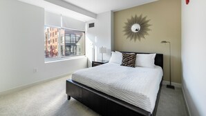 Une chambre moderne avec une grande fenêtre, un lit recouvert de linge de lit blanc, un miroir décoratif sur le mur et une lampe sur pied.