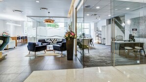Un espace de bureau moderne doté de cloisons en verre, d’un espace d’accueil avec un comptoir et des chaises, et d’un coin salon avec des canapés et une table basse.