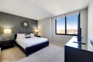 A modern hotel room with a large bed, two bedside tables with lamps, a wall-mounted mirror, and a large window offering a city view.