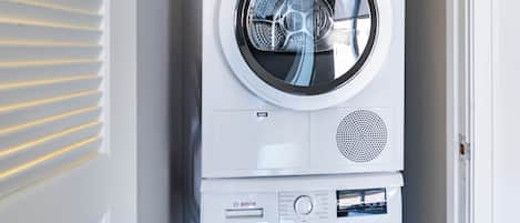 A stacked Bosch washing machine in a laundry room with a door and blinds.