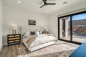 A bedroom with a bed, nightstands, a ceiling fan, a painting, and a view through a large window. - Pecan Valley 5205/5193|2 Private Pools&Spas, Private Pickleball Court, Game Room (Hurricane)